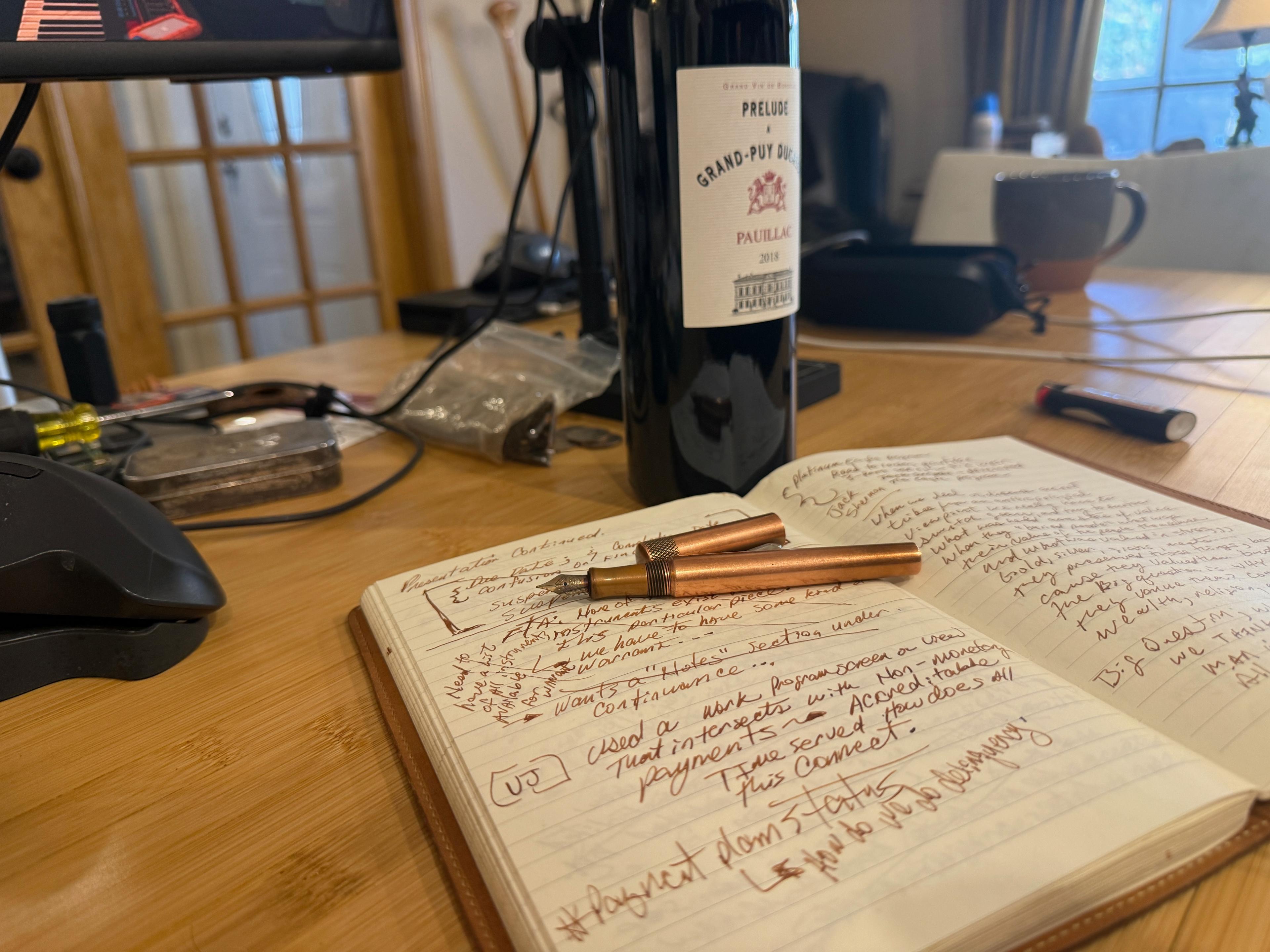 An open notebook and fountain pen beside a glass of red wine